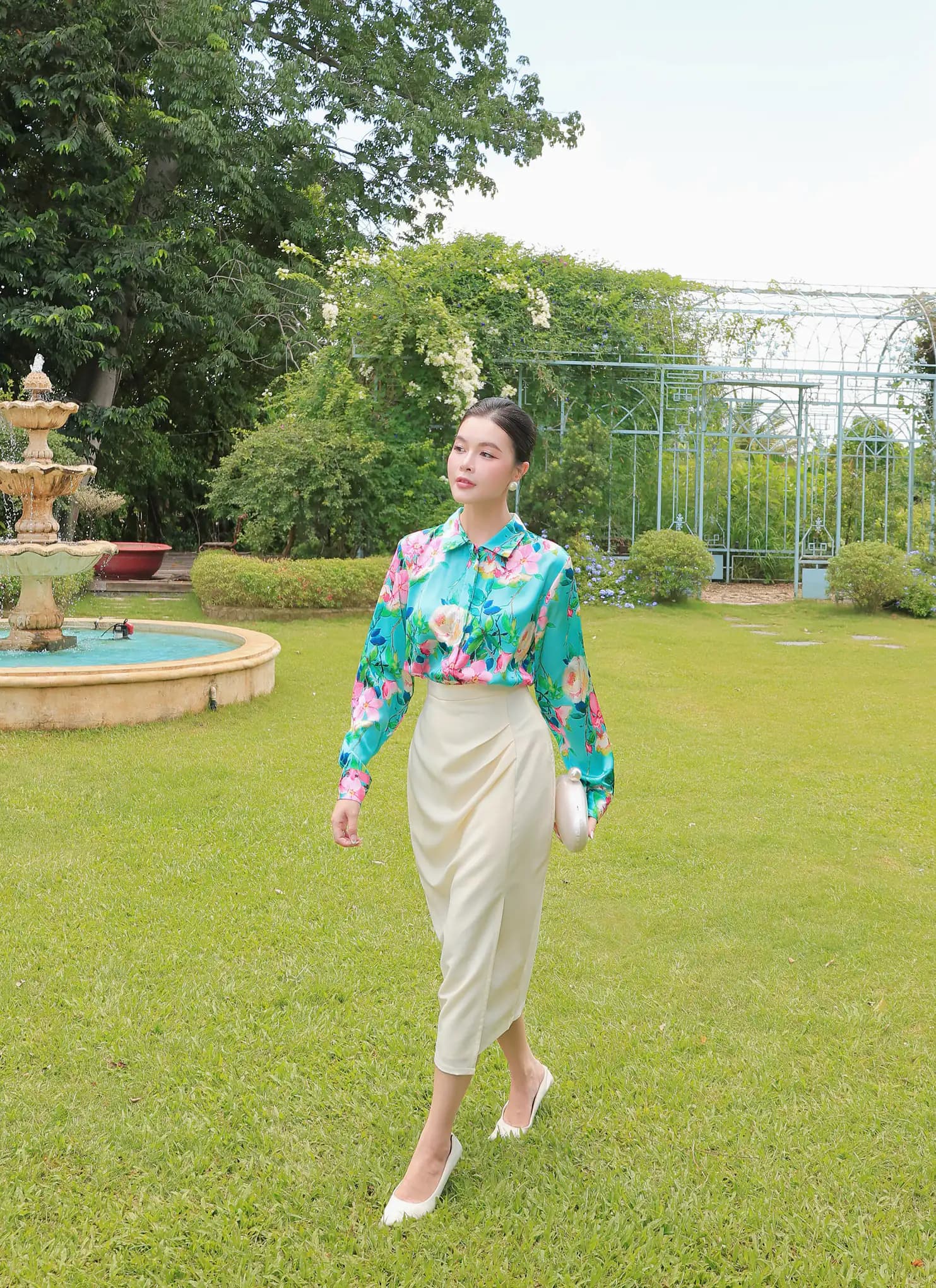 Người mẫu Maison Élégant bước giữa khu vườn và hàng cây xanh.